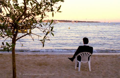 Man sitting on the beach in a tux at the Cannes Film Festival